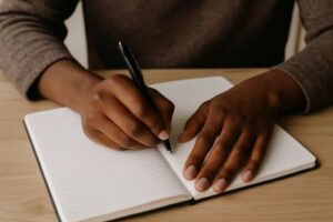 Black person journaling A black person writing in an open notebook with a black pen representing the reflective process for breaking patterns in relationships.