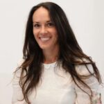 Dr. Alexandra Foglia, DMFT, smiling with long dark hair while wearing a beige jacket over a white top.
