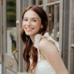 Dr. Christa Smith smiling with long reddish-brown hair while standing and wearing a white dress.