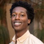 Dr. Daktari Quimby smiling while wearing a cream colored dress shirt.