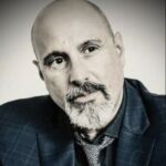 A portrait of Louis Laves-Webb sporting a dark mustache and gray beard while wearing a dark blazer and lighter tie.
