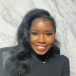 Psychotherapist Rachel Cooper seated against a white and gray background wearing a black top and a necklace, her long black hair flower over her shoulders.